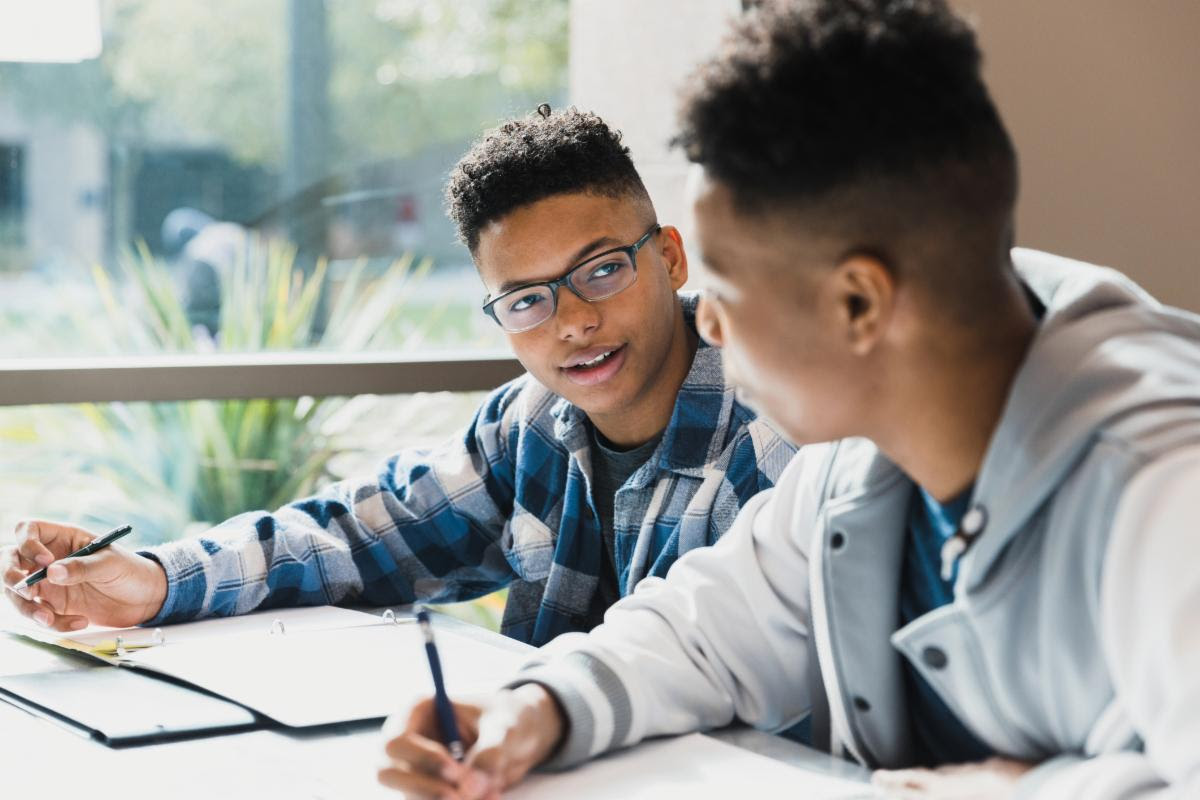 two students studying with pencils in their hands in front of window with sun shining onto their desks